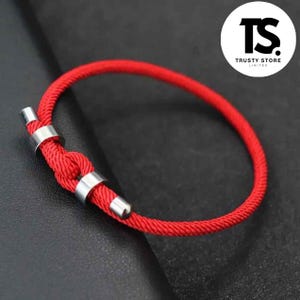 May include: A red rope bracelet with silver metal details. The bracelet is knotted in the middle and has a circular shape. The image includes a logo that says "TS TRUSTY STORE LIMITED".