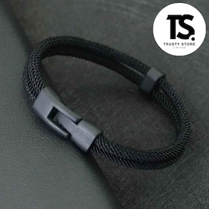 May include: A black bracelet with a woven rope design and a clasp closure. The bracelet is made of a dark material and features the text "TRUSTY STORE LIMITED" in a white circle.