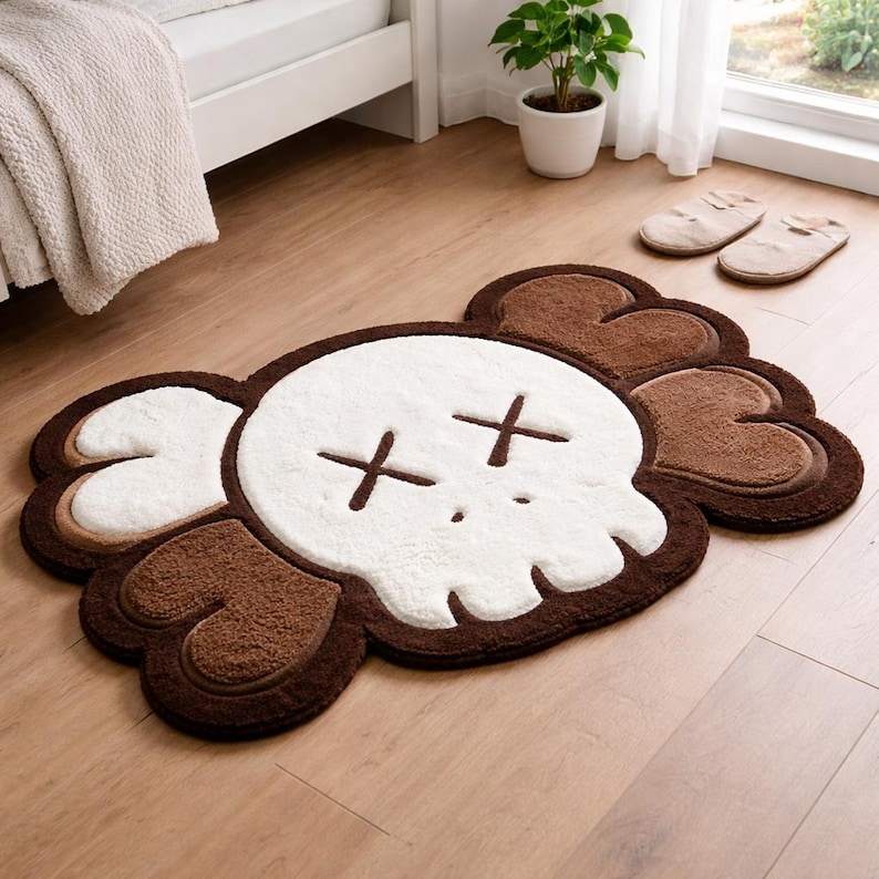 A brown, white, and tan skull-shaped rug with cross-shaped eyes. The rug has a fluffy texture and is placed on a wooden floor. The rug is a decorative item for a bedroom or living space.