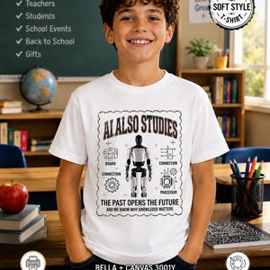 May include: A white short-sleeve t-shirt featuring a central graphic of a humanoid robot surrounded by technical diagrams and the text AI ALSO STUDIES THE PAST OPENS THE FUTURE AND WE KNOW WHY KNOWLEDGE MATTERS with labels for board and processor.