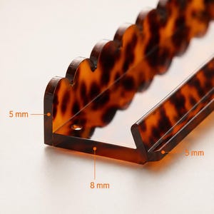 Pode incluir: Uma presilha de cabelo em acr&iacute;lico com padr&atilde;o de tartaruga e borda ondulada. A presilha tem formato de L, com espessura de 5 mm e largura de 8 mm. Projetada para manter o cabelo no lugar.