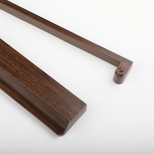 K&ouml;nnte beinhalten: Nahaufnahme eines dunkelbraunen Holzrahmens mit detaillierter Holzmaserung. Der Rahmen hat eine rechteckige Form mit einer abgerundeten Ecke und einem kleinen Stift. Der Rahmen ist vor einem wei&szlig;en Hintergrund platziert.