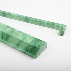 May include: Two jade green, rectangular, decorative bars with a marbled appearance. One bar has a small, cylindrical extension on the end. The bars are set against a white background. The bars appear to be made of stone.