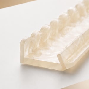 May include: A translucent, rectangular tray with a scalloped edge. The tray is made of a light beige material with a marbled effect. The design is modern and minimalist, suitable for organizing small items.