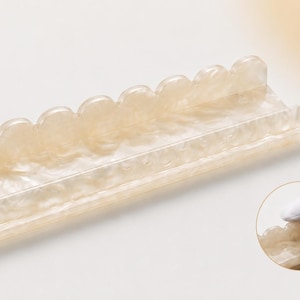 May include: A rectangular, off-white tray with a scalloped edge. The tray has a pearlescent, marbled appearance. The design is a decorative item, possibly for holding small items or as a display piece. The tray is shown on a light background.