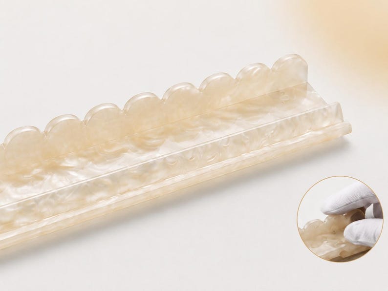 May include: A rectangular, off-white tray with a scalloped edge. The tray has a pearlescent, marbled appearance. The design is a decorative item, possibly for holding small items or as a display piece. The tray is shown on a light background.