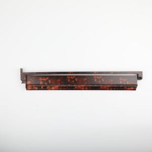 May include: A long, rectangular, tortoiseshell-patterned shelf with a dark brown frame. The shelf has a glossy finish and is mounted on a white background. The shelf is a decorative item.