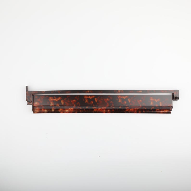 May include: A long, rectangular, tortoiseshell-patterned shelf with a dark brown frame. The shelf has a glossy finish and is mounted on a white background. The shelf is a decorative item.