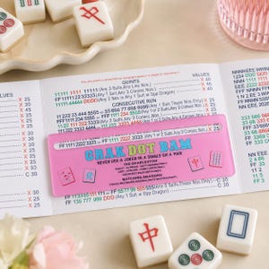 May include: A pink Mahjong card with the text "CRAK DOT BAM" and game rules is shown. Several white Mahjong tiles with red and green markings are scattered around the card. The game is played with tiles.