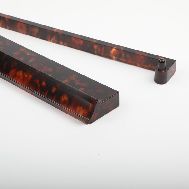 May include: Close-up of a decorative, rectangular, tortoise-shell patterned object. The object has a dark brown base with amber and black marbling. The object is angled, with a small, rounded, dark brown piece attached to the end.