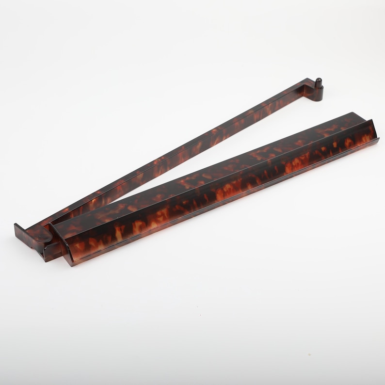 May include: A pair of vintage-style, tortoise-shell patterned serving tongs. The tongs are made of a dark brown material with lighter brown and amber marbling. The tongs are open and angled, with a rectangular base and a long, slender handle.
