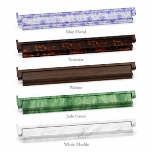 May include: A collection of five decorative trays in various styles. The trays include a blue floral design, tortoise shell, walnut, jade green, and white marble. Each tray has a rectangular shape with a raised edge and a small handle on each end.