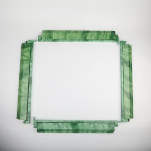 May include: A rectangular, green marble picture frame with a white interior. The frame is composed of four sections, each with a decorative, textured surface. The corners of the frame are connected with a unique interlocking design.