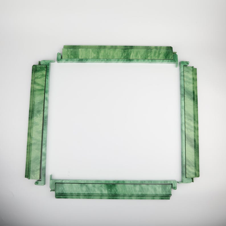 May include: A rectangular, green marble picture frame with a white interior. The frame is composed of four sections, each with a decorative, textured surface. The corners of the frame are connected with a unique interlocking design.