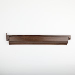 K&ouml;nnte beinhalten: Ein dunkelbraunes Holzregal mit rechteckigem Design. Das Regal hat eine erh&ouml;hte Vorderkante und ein dekoratives Endst&uuml;ck. Die Holzmaserung ist sichtbar und das Regal scheint neu zu sein.