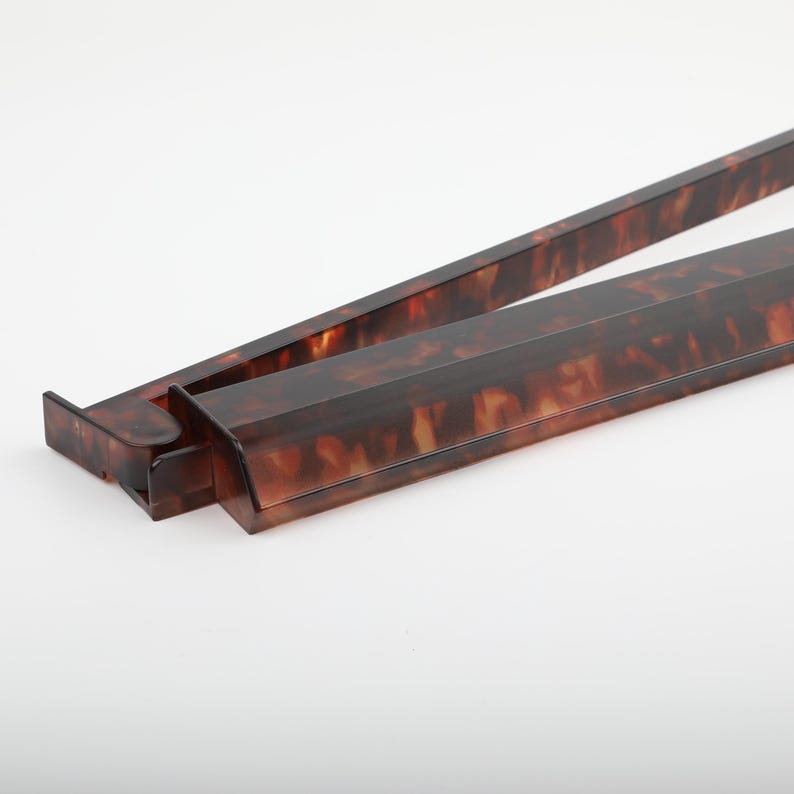 May include: A pair of serving tongs with a tortoiseshell pattern. The tongs are made of a dark brown material with lighter brown and amber marbling. The tongs are open and angled, showing the interior.