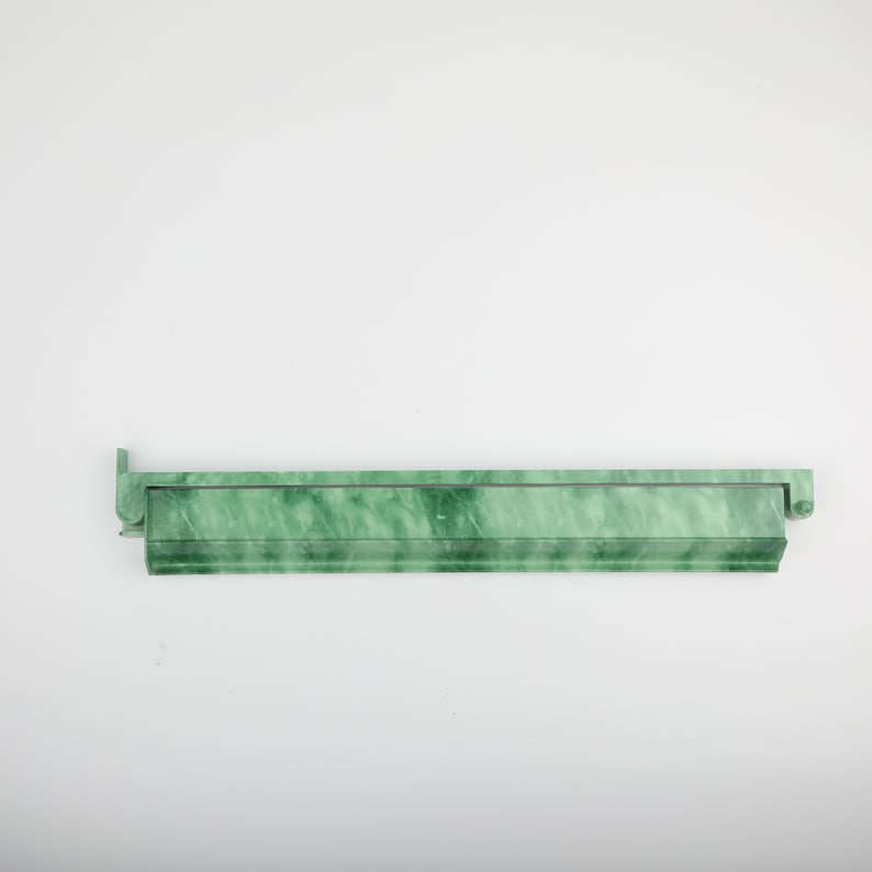 May include: A long, rectangular, green marble-look shelf with a decorative edge and a small, raised end piece. The shelf has a marbled pattern of light and dark green.