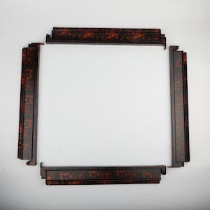 May include: Four sections of a decorative frame, arranged to form a square. The frame pieces are a dark brown with a tortoiseshell pattern. The pieces have a stepped design and are set against a white background.