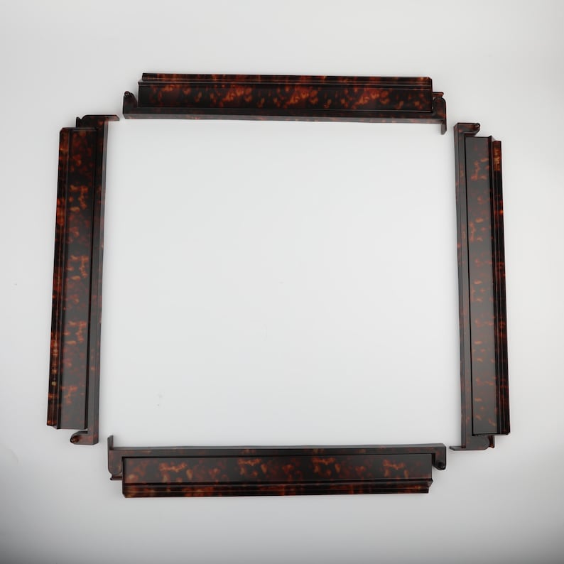 May include: Four sections of a decorative frame, arranged to form a square. The frame pieces are a dark brown with a tortoiseshell pattern. The pieces have a stepped design and are set against a white background.