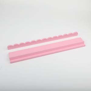 Puede incluir: Juego de estantes de madera rosa de dos piezas. El juego incluye una pieza con borde festoneado y un estante rectangular con un borde frontal elevado. Las piezas est&aacute;n pintadas de un color rosa suave y s&oacute;lido y est&aacute;n dise&ntilde;adas para montarse en la pared.