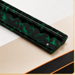 May include: A rectangular, dark green tray with a scalloped edge design. The tray has a mottled pattern of green and black, with a small circular indentation. The tray is angled against a white and beige background.