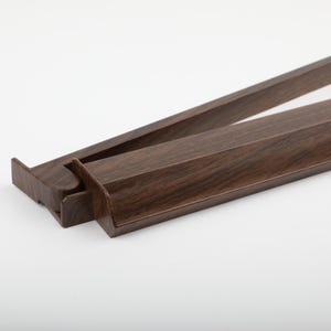 K&ouml;nnte beinhalten: Zwei braune Holz-Bilderrahmenleisten mit Holzmaserung sind vor wei&szlig;em Hintergrund schr&auml;g dargestellt. Die rechteckigen Leisten haben eine Nut an der Innenkante. Die Rahmenleisten sind f&uuml;r die Aufnahme eines Bildes oder Kunstwerks konzipiert.