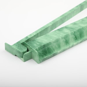 May include: A close-up of a jade green serving utensil, possibly tongs, against a white background. The utensil is made of a solid, marbled material with a rectangular shape. The tongs are open, showing the hinge and the two arms.