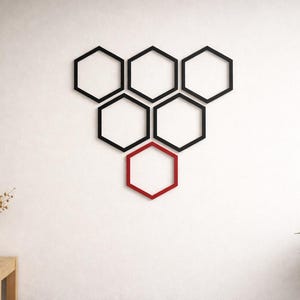 May include: A set of seven black and red hexagon-shaped shelves, designed for wall mounting. The shelves are arranged in a honeycomb pattern on a white wall. A vase of dried flowers and a potted plant are in the foreground.