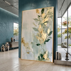 May include: A large rectangular wall art piece featuring an abstract botanical painting with gold leaf accents, sage green and dark green foliage, and a soft cream background, all encased in a thin, metallic gold frame.