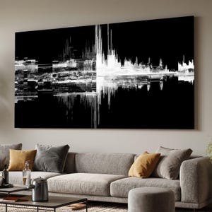 Op de afbeelding: Groot zwart-wit abstract kunstwerk. Het kunstwerk toont een grafische weergave van geluidsgolven, met een scherp contrast tussen de zwarte achtergrond en de witte lijnen. Het stuk wordt weergegeven boven een grijze bank met decoratieve kussens.