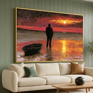Könnte beinhalten: Ein rechteckiger Wandkunstdruck in einem goldenen Rahmen, der eine einsame Figur an einem Strand bei Sonnenuntergang zeigt. Ein kleines dunkles Boot liegt im Vordergrund auf dem nassen Sand. Der Himmel ist mit tiefroten und orangen Wolken gefüllt.