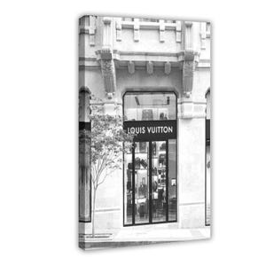 May include: Black and white photograph of a Louis Vuitton store front. The store has a large glass window displaying handbags and other merchandise. The building has ornate architectural details and a small tree in front.