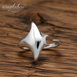 May include: A polished silver ring with a distinctive, angular design. The ring has a central, pointed shape with curved details. The ring is displayed on a wooden surface, and the brand name "ringlabco" is visible in the upper left corner.