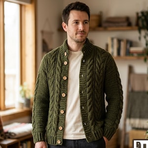 Puede incluir: Un cárdigan de punto trenzado en color verde oliva con cuello alto, mangas largas y cierre frontal de botones circulares claros. La prenda se lleva sobre una camiseta blanca lisa y pantalones de color gris oscuro, mostrando un patrón texturizado.