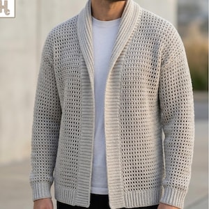 Op de afbeelding: Een lichtbeige open vest met een gestructureerd haakpatroon, een brede sjaalkraag en geribbelde boorden. Het kledingstuk wordt gedragen over een effen wit t-shirt en toont een consistent weefpatroon over de mouwen en het lichaam.
