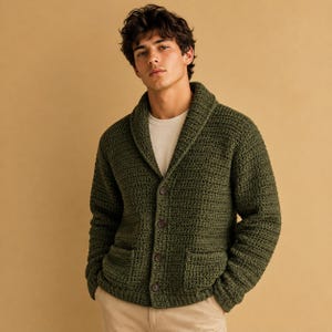 Könnte beinhalten: Eine dunkelolivgrüne Langarm-Strickjacke mit dickem Schalkragen, einem strukturierten Häkelmuster, vier dunkelbraunen Knöpfen auf der Vorderseite und zwei quadratischen aufgesetzten Taschen in der Taille, getragen über einem schlichten weißen T-Shirt.