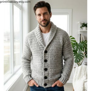 Könnte beinhalten: Hellgraue Häkelstrickjacke mit Knöpfen und Schalkragen. Der Pullover hat große, dunkle Knöpfe und wird über einem weißen Hemd getragen. Der Etsy-Shop-Name "printhivecozy.etsy.com" ist oben links sichtbar.