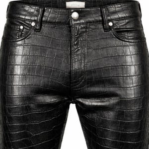 Puede incluir: Primer plano de unos pantalones de cuero negro con textura de piel de cocodrilo. Los pantalones tienen cierre de botón y dos bolsillos delanteros. Los pantalones son de color oscuro liso.