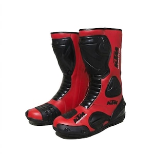 Könnte beinhalten: Paar rote und schwarze Motorradstiefel. Die Stiefel haben ein hoch geschnittenes Design mit schwarzen Akzenten an Schienbein, Knöchel und Zehen. Das KTM Racing Team-Logo ist auf der Seite jedes Stiefels sichtbar.