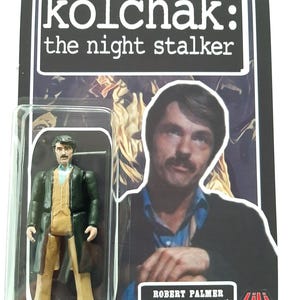 Puede incluir: Una figura de acción de un hombre con bigote que viste un abrigo verde oscuro, un chaleco beige y una camisa azul claro. La figura está dentro de un blíster de plástico transparente sobre un cartón con el texto Kolchak: The Night Stalker.