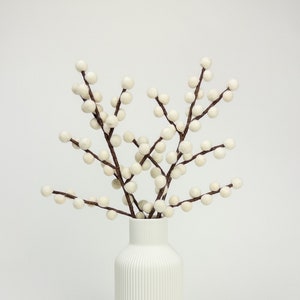 May include: White vase with a textured surface, filled with white berry branches.