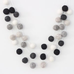 May include: A garland of felt balls in black, white, and gray. The balls are strung on white thread and are arranged in a cascading pattern.