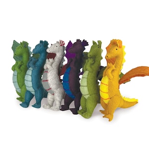 Puede incluir: Un conjunto de siete juguetes de dragón de fieltro en varios colores, incluyendo verde, azul, gris, morado, amarillo y naranja. Los dragones están de pie con las alas extendidas.
