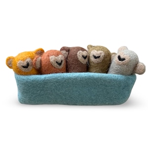 May include: A felt sculpture of five monkey heads in shades of yellow, orange, brown, olive green, and grey. They are in a light blue felt boat-shaped container. Each monkey has a heart-shaped face and black eyes.