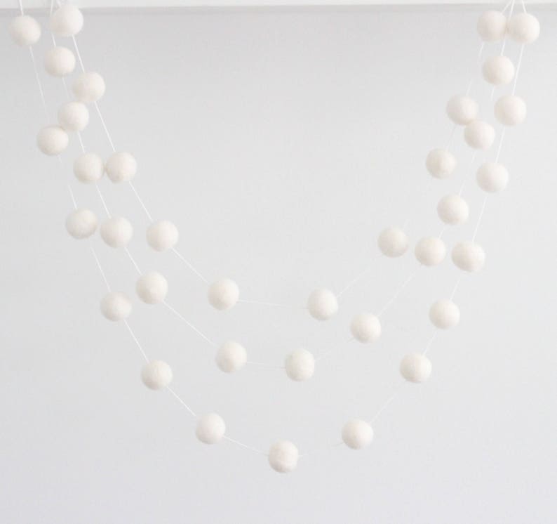 May include: A white felt ball garland with multiple strands of balls hanging from a white background.