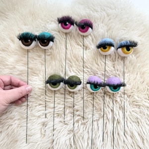 Peut inclure: Un ensemble de dix yeux en feutre avec des cils sur des tiges de fil. Les yeux sont de diff&eacute;rentes couleurs, notamment le violet, le vert, le bleu et le rose.