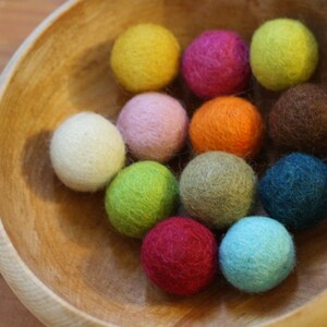 May include: A wooden bowl filled with colorful felt balls. The balls are in various shades of pink, green, blue, yellow, orange, brown, and beige.