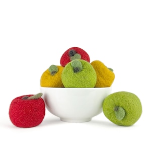May include: A white bowl filled with felt apples in red, green, and yellow colors. The bowl is sitting on a white surface.