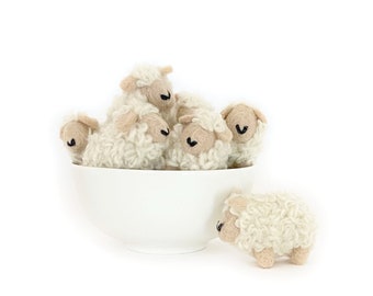 May include: A white ceramic bowl filled with five small, fluffy, white sheep figurines. One sheep is peeking out from the bowl.