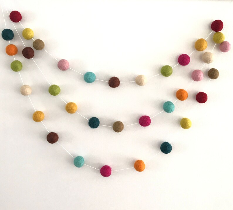 May include: A colorful felt ball garland with a variety of colors, including red, orange, yellow, green, blue, purple, and brown. The garland is strung on a white string and is perfect for adding a touch of whimsy to any room.